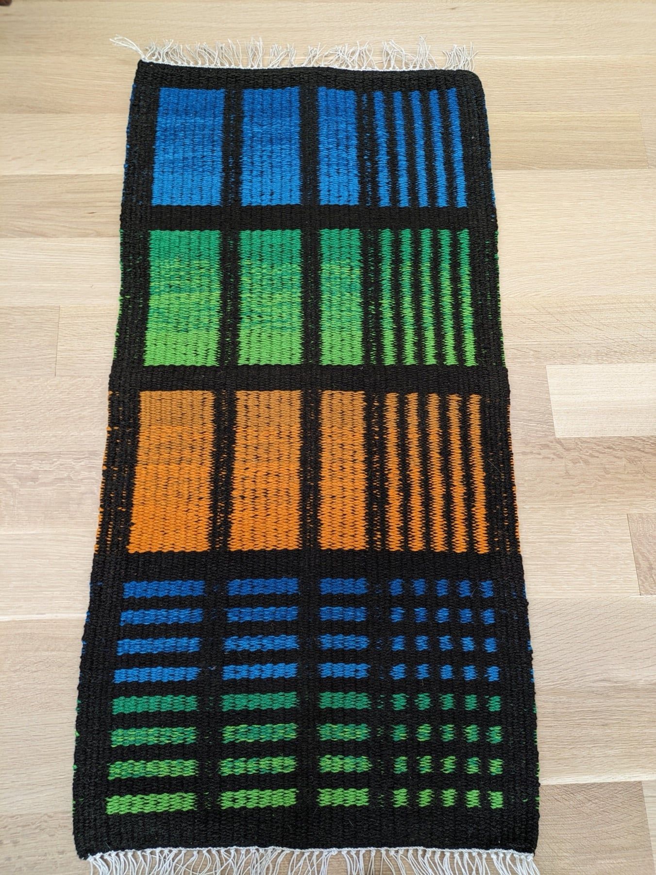 A woven rug in blocks of blue, green and orange on black