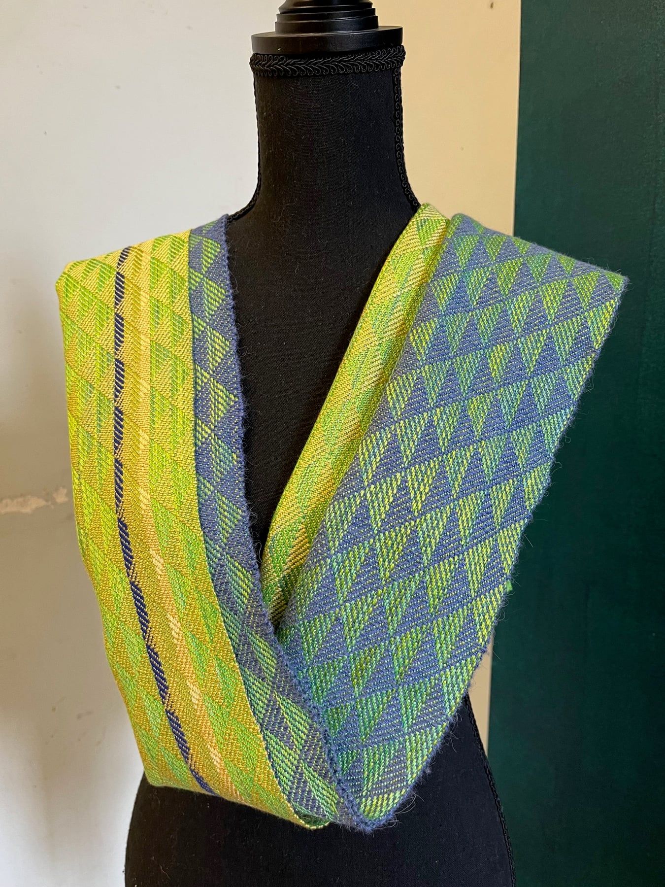 A scarf woven in green, yellow and blue triangles, draped on a dress form